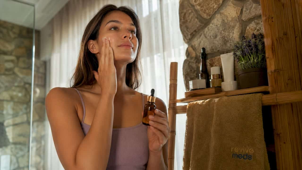 Woman applying GHK-Cu serum to face in bathroom